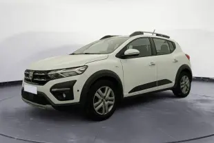Vue 3/4 avant droit d'une Dacia Sandero blanche avec barres de toit et protections noires sur les bas de caisse.
