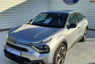 Citroën C4 gris vue 3/4 avant droit, avec calandre distinctive et jantes bi-ton, stationnée devant un mur blanc.