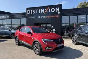 Renault Arkana rouge flamme métal vu en 3/4 avant droit, avec jantes alliage grises 17 pouces, stationné devant un showroom.