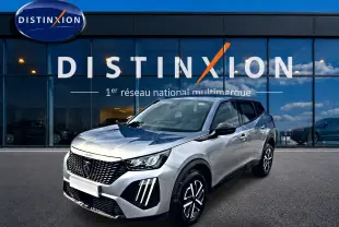 Peugeot 2008 gris en 3/4 avant droit, avec calandre noire et feux LED distinctifs, devant une vitrine Distinxion.
