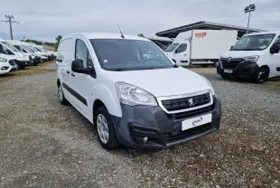 Peugeot Partner blanc en 3/4 avant droit, avec pare-chocs noir et calandre distinctive, stationné sur un sol gravillonné.
