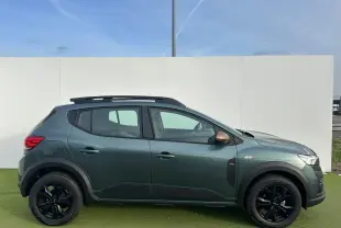 Profil droit de la Dacia Sandero III Stepway vert cèdre avec jantes noires et barres de toit brun cuivré.