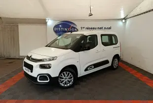 Vue 3/4 avant droite du Citroën Berlingo blanc avec protections latérales noires et jantes alliage en intérieur showroom.
