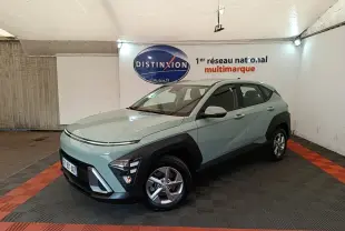 Vue 3/4 avant droite d’un Hyundai Kona 2024 vert clair avec protections noires et jantes alliage en intérieur showroom.