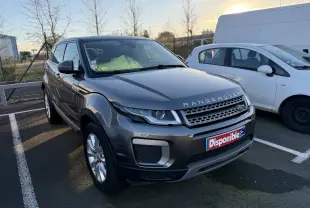 Range Rover Evoque gris vue 3/4 avant droit, avec calandre distinctive et plaque "Disponible" sur parking extérieur.