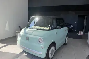 Vue 3/4 avant d'une Fiat 124 Spider Topolino 2024 bleu clair électrique avec toit noir en intérieur showroom.