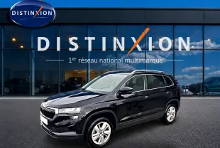 SKODA KAROQ noir 2025 en 3/4 avant droit, avec jantes alu et barres de toit visibles devant un showroom Distinxion.