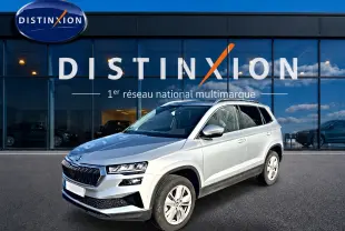 Vue 3/4 avant droite d'un Skoda Karoq gris 2025 devant une vitrine Distinxion, avec calandre noire et jantes alu.