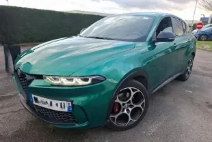 Vue 3/4 avant d'une Alfa Romeo Tonale 1.5 MHEV 130 TCT7 vert foncé avec jantes distinctives en intérieur showroom.