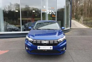 Vue avant d'une Dacia Sandero 2025 bleu Iron avec signature lumineuse LED et feux antibrouillard, stationnée devant un bâtiment.