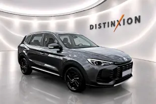 Vue 3/4 avant droite d’un MG ZS gris foncé hybride 2026 avec calandre noire et phares LED, devant un bâtiment industriel.