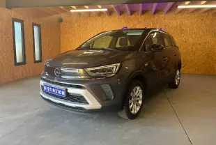 Opel Crossland gris en 3/4 avant droit, avec calandre chromée et jantes alliage dans un garage en bois.