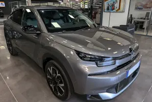 Citroën C4 hybride gris Mercury vue 3/4 avant droit en intérieur, avec jantes biton et calandre distinctive.