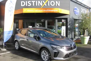 Renault Clio V gris schiste vue 3/4 avant droit, garée devant un showroom Distinxion avec calandre distinctive.