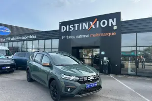 Vue 3/4 avant d'un Dacia Jogger kaki lichen métal avec calandre noire et jantes noires devant un concessionnaire Distinxion.