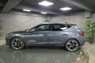 Vue de profil côté gauche d'une CUPRA Leon gris magnétique avec jantes alliage 18'' dans un showroom intérieur.