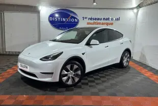 Tesla Model Y blanc en 3/4 avant droit dans un showroom avec sol noir et orange et logo Distinxion en arrière-plan