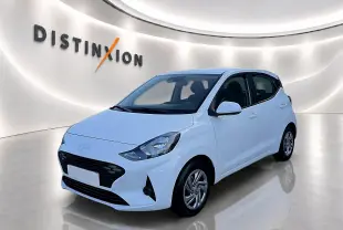 Vue 3/4 avant d'une Hyundai i10 blanche 2024 avec enjoliveurs et rétroviseurs assortis en intérieur showroom lumineux.