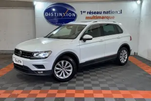 Volkswagen Tiguan blanc vu de 3/4 avant droit dans un showroom avec jantes alliage et barres de toit noires.