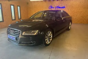 Audi A8 3.0 TDI noire vue en 3/4 avant droit dans un showroom avec éclairage chaud et murs en bois.