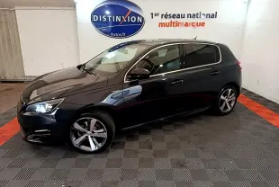 Peugeot 308 gris foncé vue de profil droit en intérieur, avec jantes alliage et phares allumés.