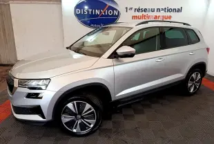 Vue 3/4 avant droite d’un Skoda Karoq gris clair 2022 avec jantes alliage et barres de toit noires.