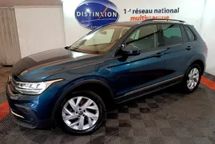 Vue 3/4 avant droit d'un Volkswagen Tiguan bleu hybride rechargeable, avec jantes alliage et prises de recharge visibles.