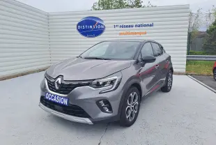 Renault Captur gris Cassiopée avec toit noir, vue 3/4 avant droit, sur parking devant un mur blanc.