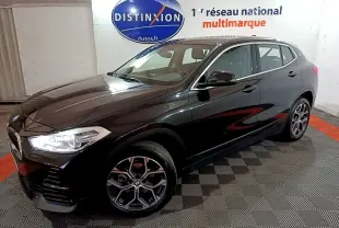 BMW X2 sDrive18i Lounge noir en 3/4 avant droit, avec jantes alliage et phares LED allumés.