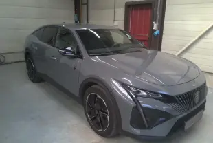 Peugeot 408 gris selenium vue 3/4 avant droit, avec calandre noire distinctive et jantes bi-ton.