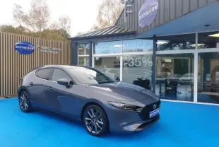 Vue 3/4 avant gauche de la Mazda3 2024 Platinum Quartz Métallisé garée devant un showroom Distinxion.