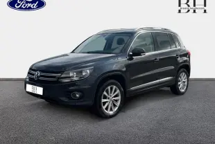 Volkswagen Tiguan gris poivre vu en 3/4 avant droit avec jantes alu et barres de toit visibles.