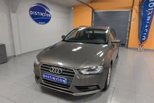 Audi A4 gris 3/4 avant droit en intérieur, avec plaque et signalétique Distinxion visibles sur le mur et au sol.