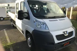 Vue 3/4 avant gauche d'un utilitaire blanc Peugeot Boxer Chassis Double Cabine avec plateau et sept places visibles.