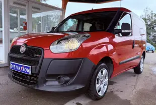 Fiat Doblo Cargo rouge en 3/4 avant droit, avec pare-chocs noir et phares allumés sous abri.