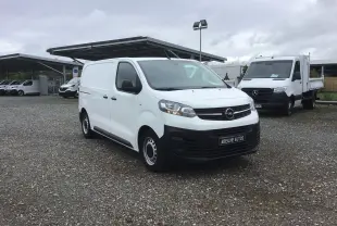 Fourgon Opel Vivaro blanc vu en 3/4 avant droit sur un parking avec d'autres véhicules utilitaires.