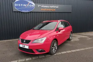 SEAT Ibiza ST rouge vue 3/4 avant droit, avec jantes alliage et phares Xenon, stationnée devant un mur noir.