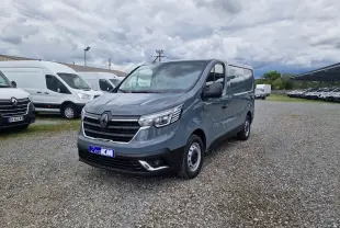 Renault Trafic Fourgon gris urbain vu en 3/4 avant droit sur un parking avec plusieurs utilitaires blancs en arrière-plan.