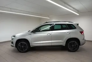 Vue de profil côté gauche d’un Skoda Karoq gris argent 2025 avec toit panoramique et jantes noires en intérieur neutre.