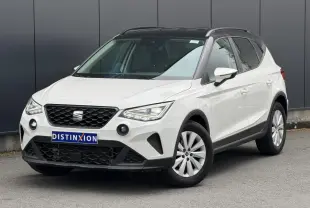 Vue 3/4 avant droite d'un SEAT Arona blanc avec toit noir et jantes alliage 16 pouces, garé devant un mur gris.