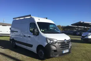 Renault Master blanc en 3/4 avant droit avec galerie de toit et pare-chocs noir visible sur parking extérieur.