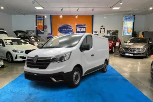 Renault Trafic Fourgon blanc en 3/4 avant droit, présenté en showroom sur tapis bleu avec autres véhicules autour.