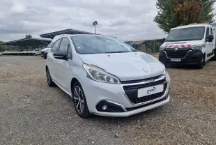 Peugeot 208 blanc nacré vue 3/4 avant droit, avec jantes alliage bicolores et calandre chromée, stationnée sur sol gravillonné.