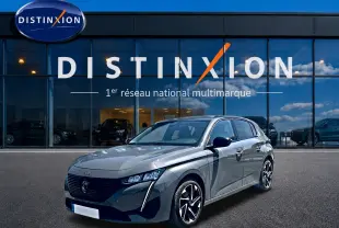 Peugeot 308 gris vue 3/4 avant droit, avec phares LED et jantes alliage distinctives, devant showroom Distinxion.