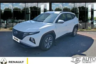 Hyundai Tucson blanc en 3/4 avant droit, avec calandre noire et jantes alliage visibles, stationné devant un bâtiment vitré.