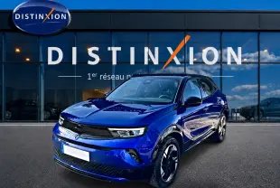 Opel Mokka Electric 156 gs bleu en 3/4 avant droit devant une vitrine avec logo Distinxion.