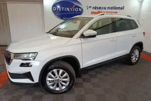 Vue 3/4 avant droite d'un Skoda Karoq blanc 2024 avec jantes alliage et barres de toit noires en showroom