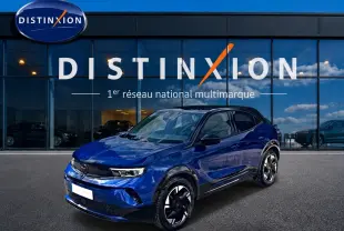 Opel Mokka Electric bleu en 3/4 avant droit, avec jantes alu noires et toit noir devant showroom Distinxion.