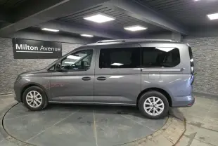 Vue de profil côté gauche d'un Ford Transit Connect gris 2023 avec portes coulissantes et barres de toit argentées.
