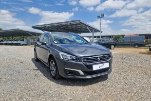 Peugeot 508 SW gris shark vue 3/4 avant droit sur un parking avec abris solaires en arrière-plan.